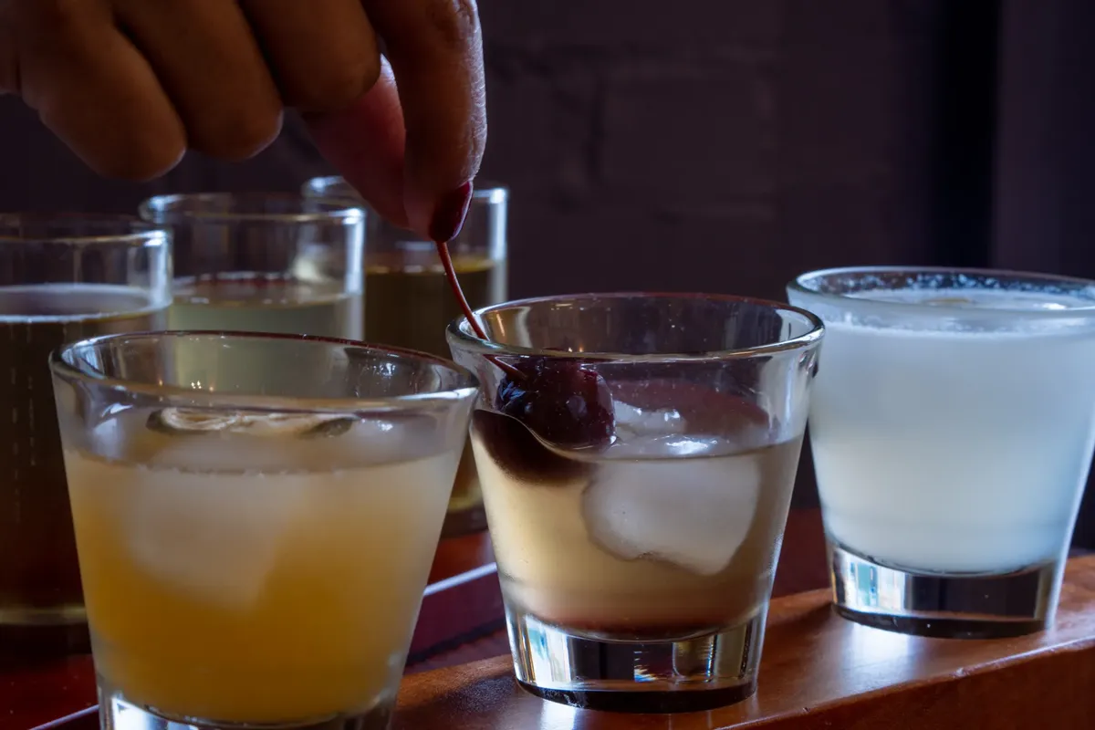 A selection of refreshing cocktails with a hand garnishing a cherry, perfect for beverage enthusiasts.
