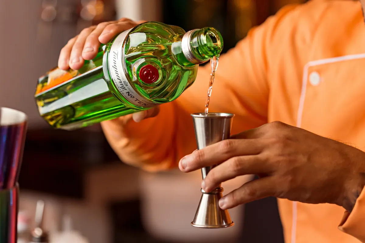 Close-up of a bartender pouring gin into a jigger, preparing a cocktail.